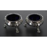 Pair of George III silver salt cellars, with blue glass liners, repousse decorated with flowers