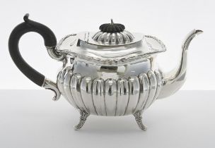 George V silver teapot, with a hardwood handle and half gadrooned body raised on four scaled feet,