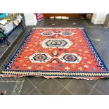 An Aztec Design Woolen Rug, Red Salmon Ground, Geometric Blue And White Border, 310 x 255 cm.