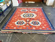 An Aztec Design Woolen Rug, Red Salmon Ground, Geometric Blue And White Border, 310 x 255 cm.