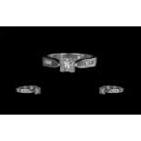 A Platinum Diamond Engagement Ring, set with a central princess cut diamond, four round cut