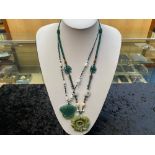 Two Green Jade Pendant Necklaces, one having a large, carved, floral pendant, on a thread necklace