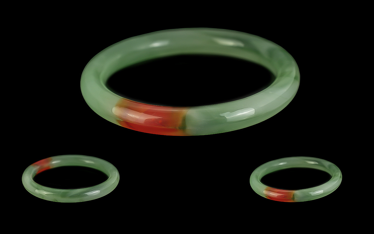 A Jadeite Bangle of Celadon to Bright Green Colour, With Red Section. Mid 20th Century. Weight 38.