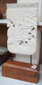 An Indonesian sandstone carving of a mask, bird and flowers on hardwood stand, 62.5cms high Height