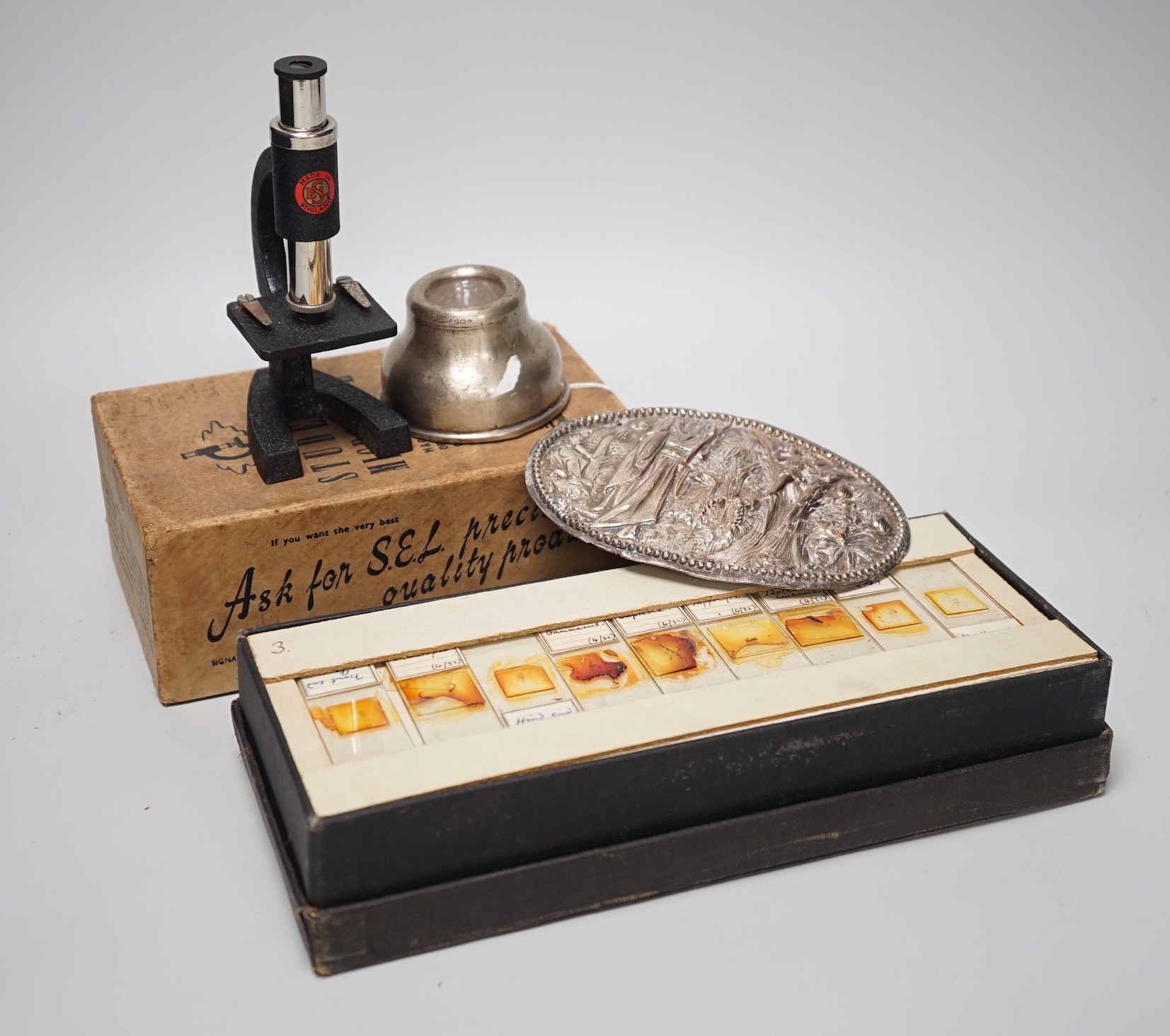 A case of early 20th century microscopes slides and a student's microscope, a small silver inkwell