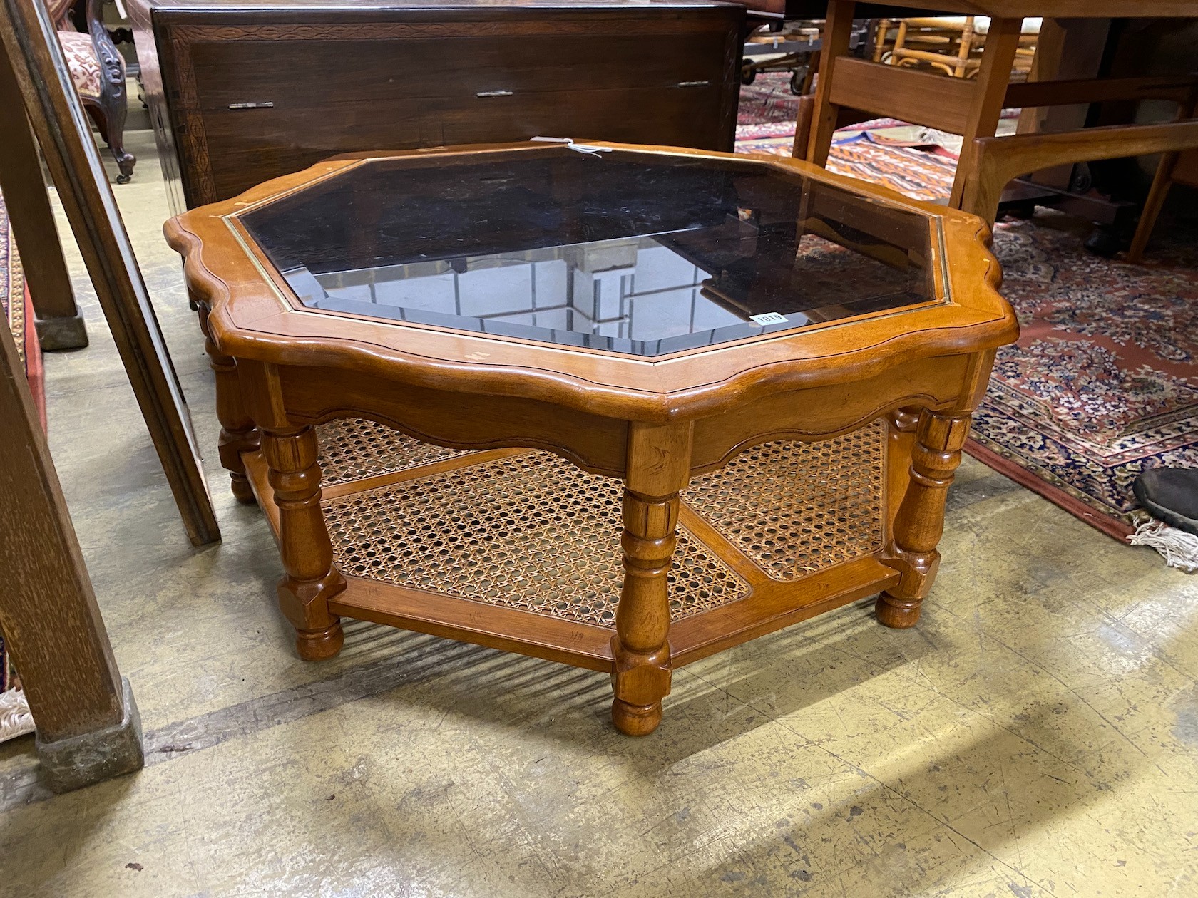 A modern octagonal brass mounted walnut glass top coffee table with caned undertier, diameter 100cm,