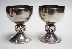 A stylish pair of Elizabeth II Arts & Crafts style planished silver pedestal cups, with