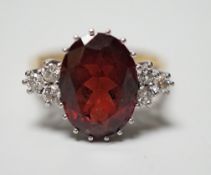 A modern 18ct gold and oval cut garnet set dress ring, with six stone diamond set shoulders, size