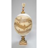 A decorated ostrich egg on gilt stand with a gilt and seed finial, 27cms high