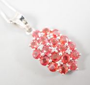 A modern 375 white metal, sunset ruby and white sapphire set cluster pendant, 19mm, on a 375 white