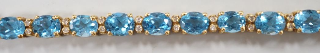 A modern 750 yellow metal and blue topaz set line bracelet, with diamond chip spacers, 17.75cm,