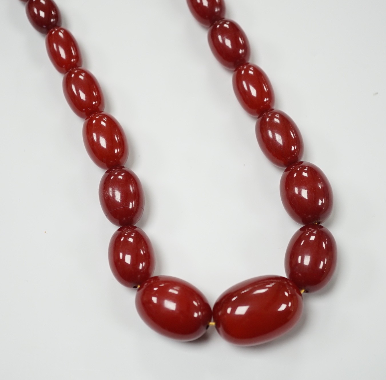 A single strand graduated simulated oval cherry amber necklace, 82cm, gross weight 113 grams.