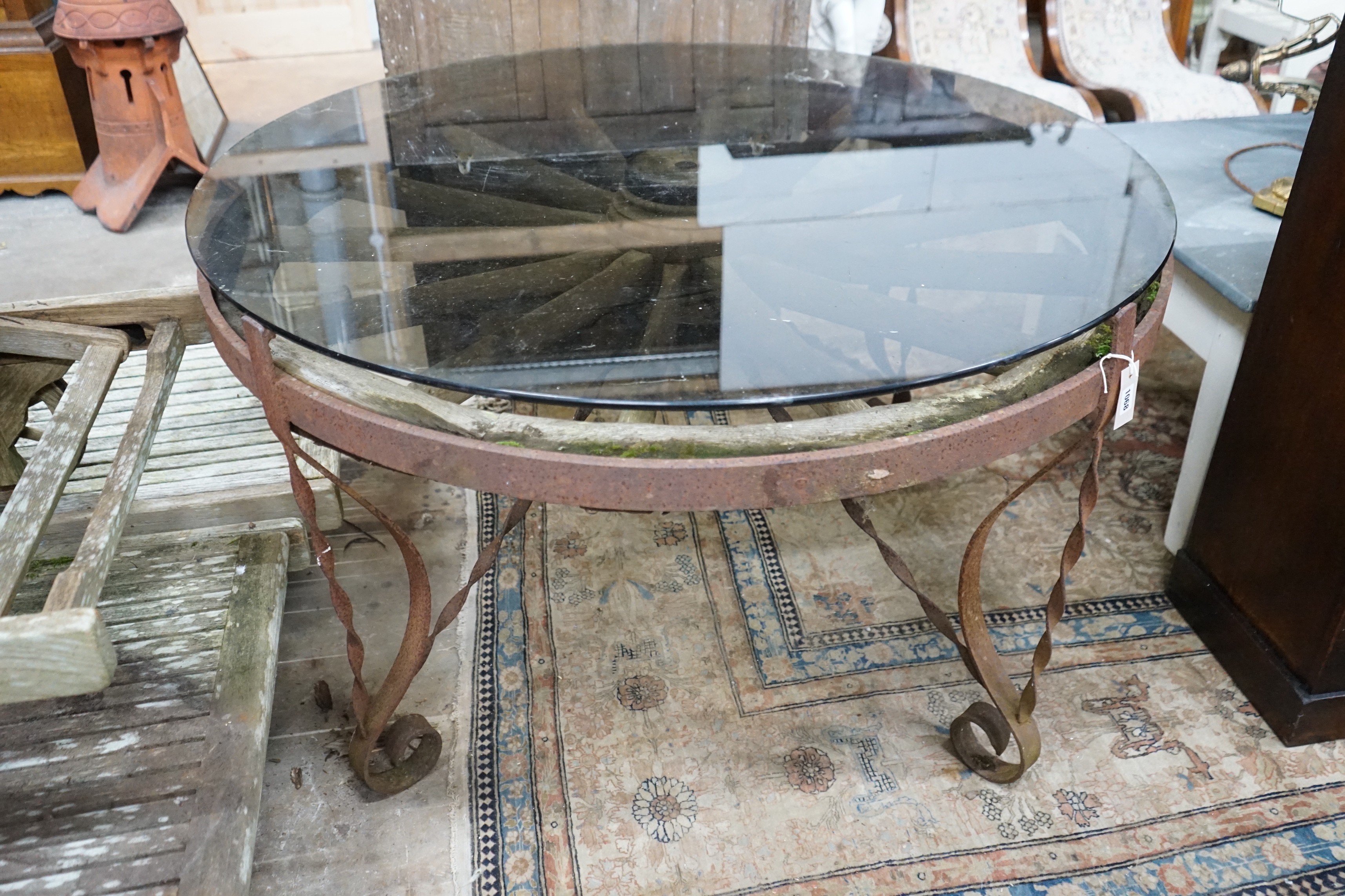 A wrought iron glass topped circular cartwheel garden table, diameter 124cm, height 72cm