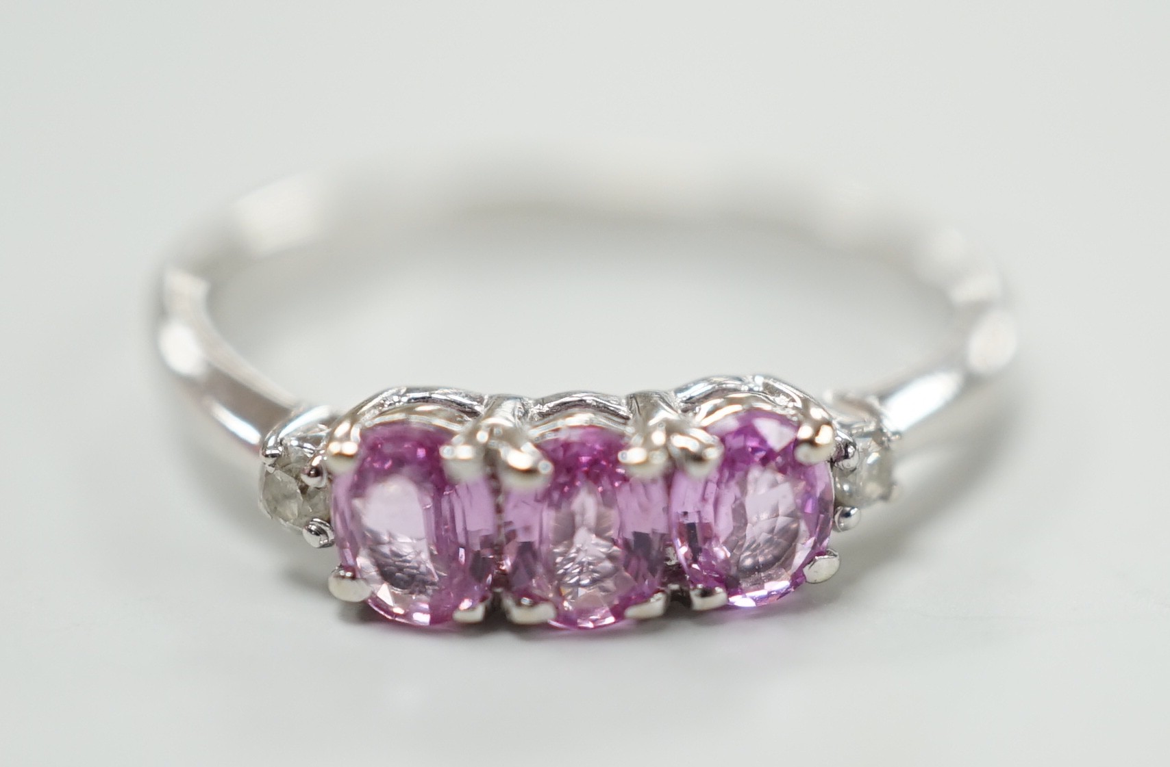 A modern 14ct white gold, three stone pink sapphire and two stone diamond chip set ring, size L,