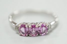 A modern 14ct white gold, three stone pink sapphire and two stone diamond chip set ring, size L,