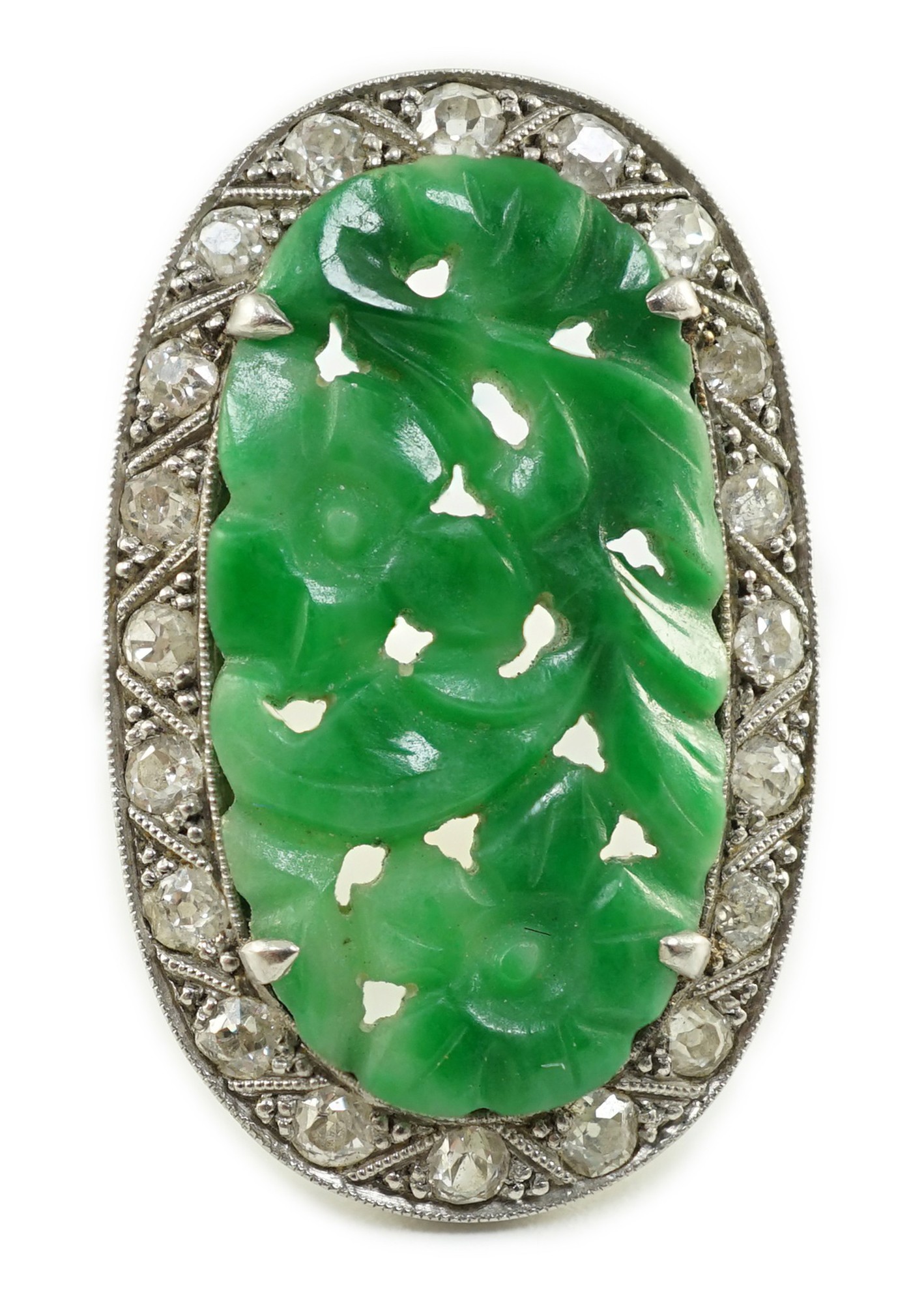 A 1920's/1930's white gold, jadeite and diamond set oval dress ring, the foliate carved jadeite,