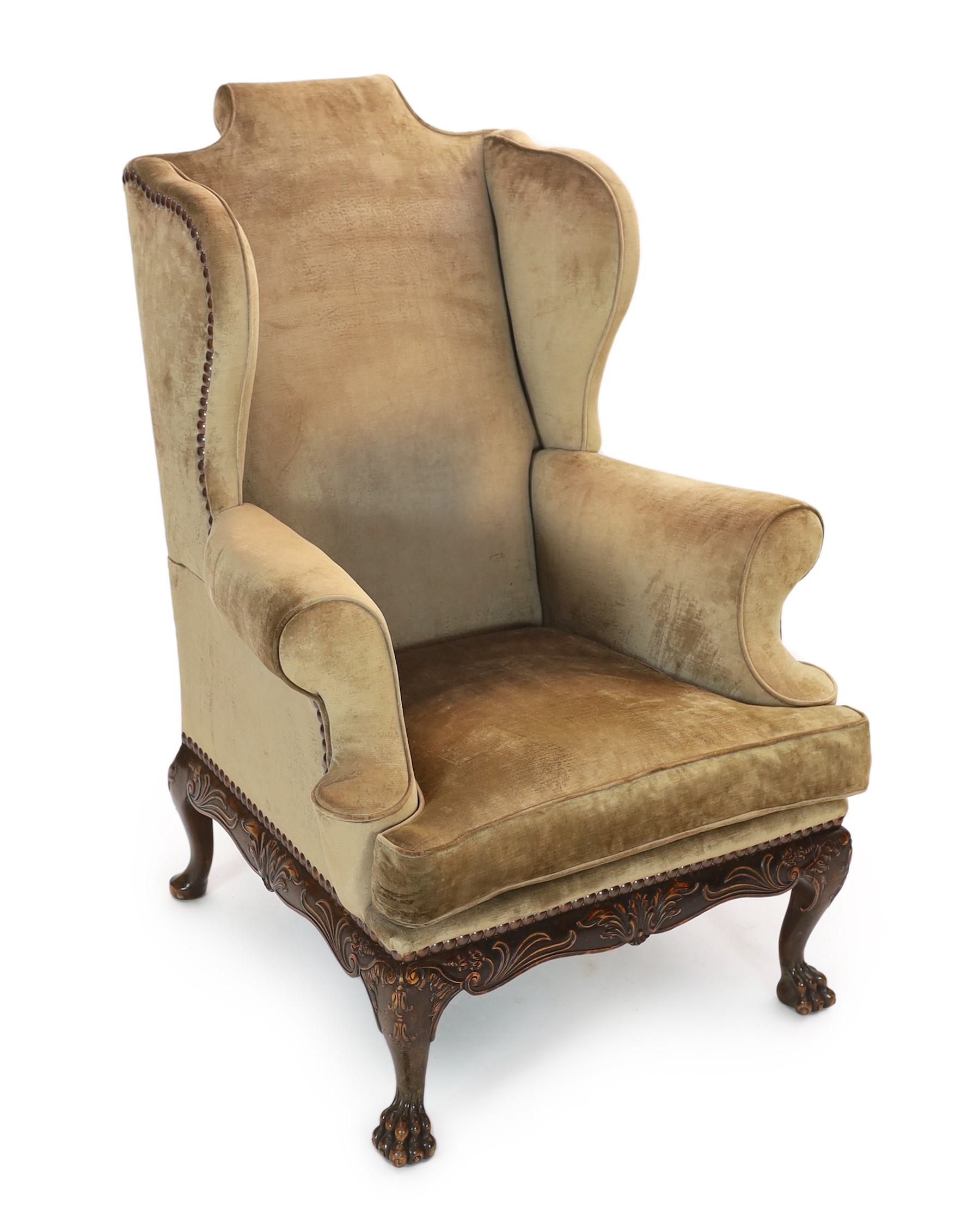 An Irish mahogany wing armchair, in George III style, with foliate scroll carved apron, on