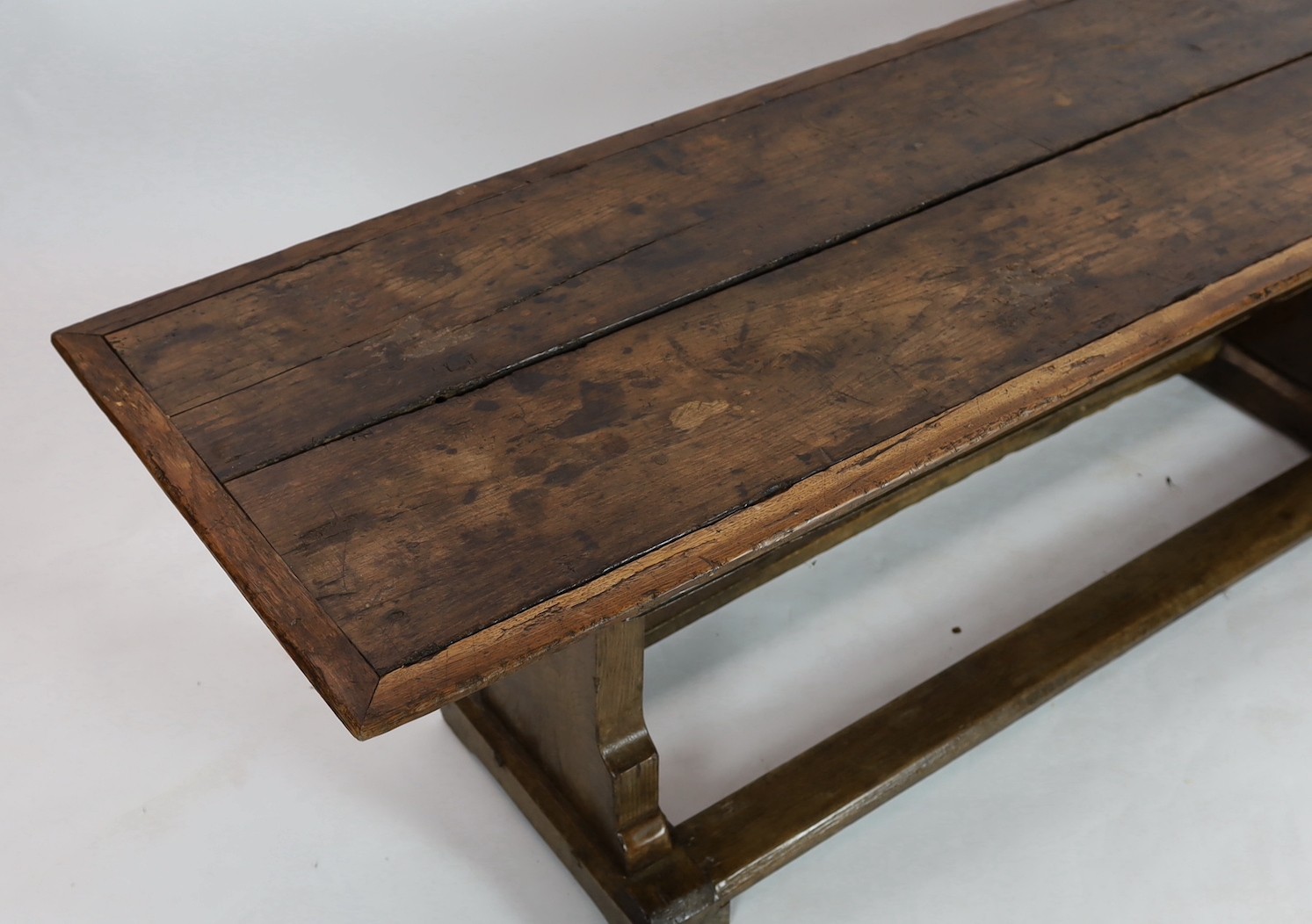 A narrow oak refectory table, part 17th century, the cleated twin plank top above trestle supports - Image 2 of 4