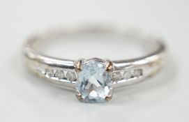 A modern 9ct white gold and oval cut blue topaz ring, with diamond chip set shoulders, size N, gross