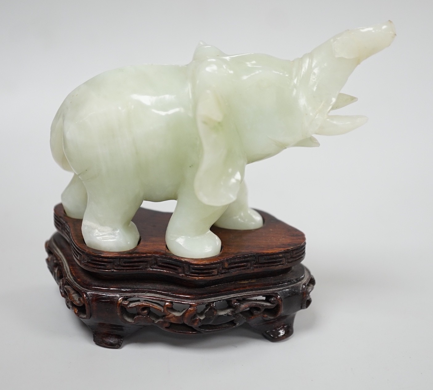 A Chinese bowenite jade elephant on hard wood stand, 11cm tall