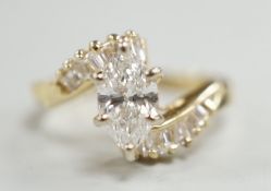 A yellow metal and singe stone marquise cut diamond set crossover dress ring, with baguette cut