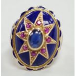 A yellow metal, blue enamel, ruby and cabochon sapphire set oval dress ring, the shank inscribed '