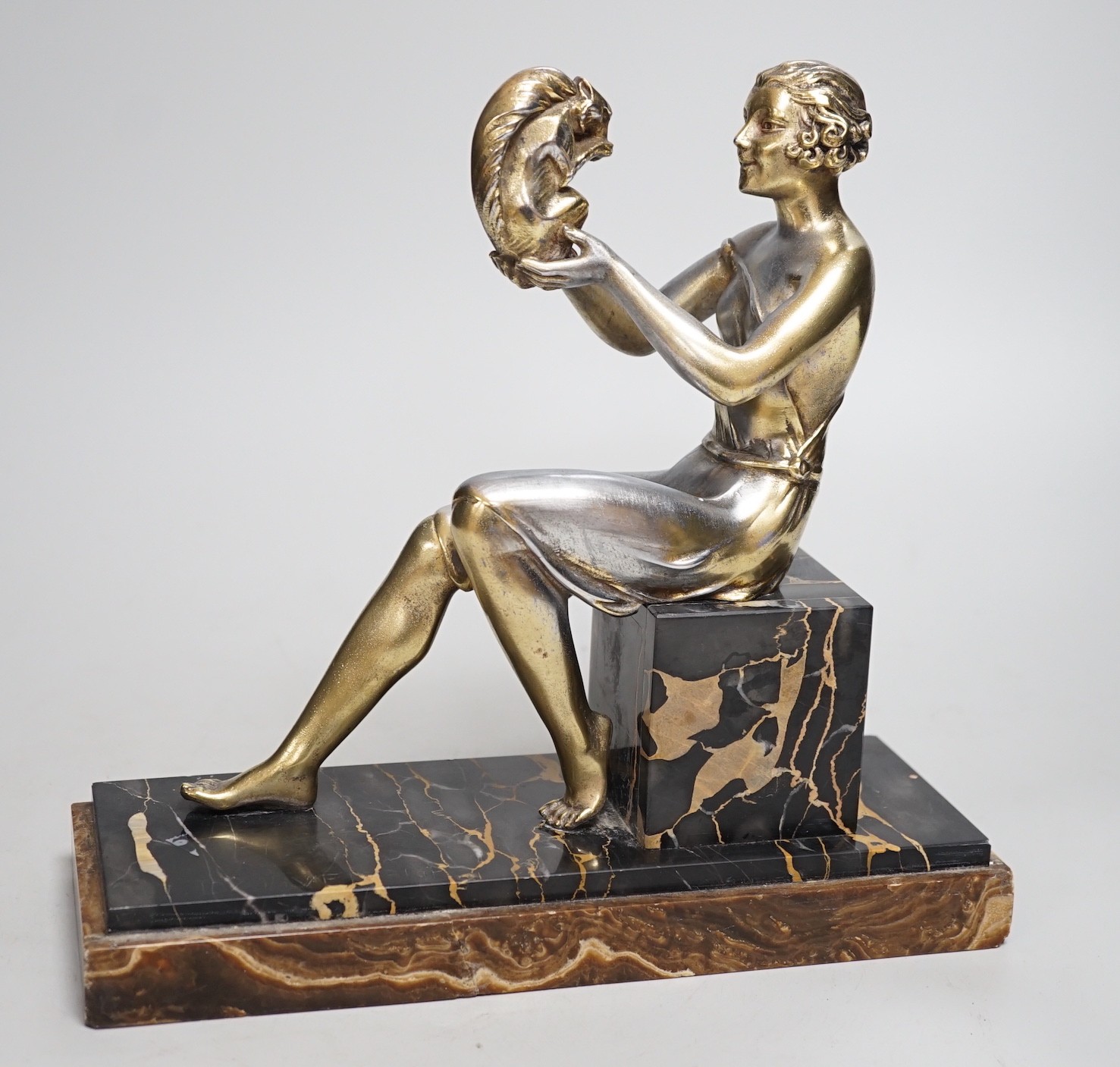 An Art Deco spelter gilded and silvered seated lady holding a squirrel, on marble and onyx mount,