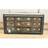 An early 20th century painted nine drawer spice hanging cupboard, 62cms wide, 31cms high