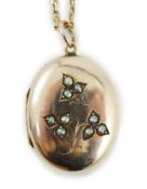 An Edwardian yellow metal and seed pearl set oval locket pendant, 25mm, on a 9ct chain, 47cm,