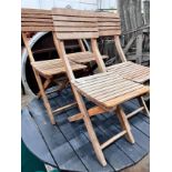 A grey stained teak circular garden table and four faded teak folding chairs, table diameter