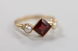 An early 20th century yellow metal, single stone garnet and two stone split pearl set ring, size
