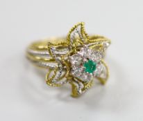 A yellow and white metal, emerald and diamond cluster set stylised flower head ring, size P, gross