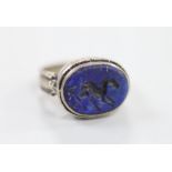 An engraved white metal and intaglio lapis lazuli set oval ring, the matrix carved with a horse?