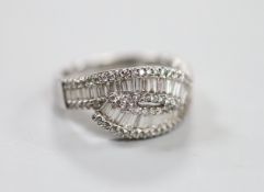 A modern 18ct white gold, baguette cut and diamond chip cluster set crossover ring, size O, gross
