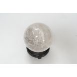 A rock crystal quartz sphere, probably from Brazil, on a carved wood stand, 10cm tall