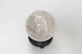 A rock crystal quartz sphere, probably from Brazil, on a carved wood stand, 10cm tall