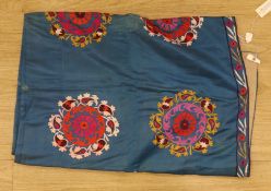 An early 20th century Suzani hanging, embroidered with red pink and gold foliate designs, on blue