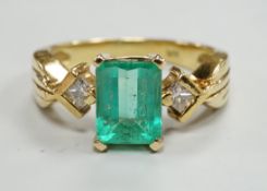 A modern 18k yellow metal and single stone emerald set ring, with two stone diamond set shoulders,