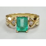A modern 18k yellow metal and single stone emerald set ring, with two stone diamond set shoulders,