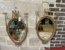 A pair of Edwardian Adam design giltwood and composition oval wall mirrors with swagged urn