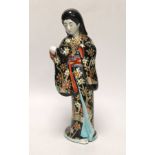 A Japanese porcelain figure of a geisha girl wearing a floral blue ground kimono, 27cm tall