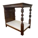 A 17th century style oak tester bedstead, with gadrooned panelled canopy on cup and cover front