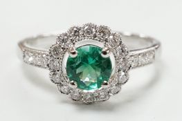 A modern 18ct white gold, emerald and diamond set circular cluster ring, with diamond set shoulders,