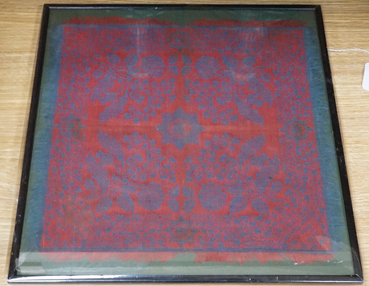 An unusual framed George IV Irish damask napkin, designed with a red ground and blue woven floral
