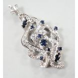 A modern 18k white metal sapphire and diamond chip cluster set scroll pendant, overall 47mm, gross