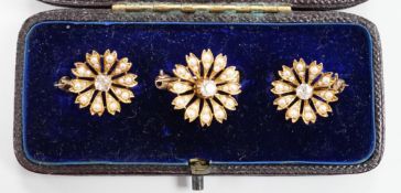 A cased graduated set of three Edwardian yellow metal, seed pearl and diamond set flower head