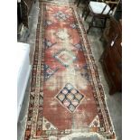 An Antique Caucasian brick red ground runner 336cm x 110cm, severely worn and holed