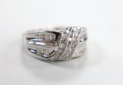 A modern 14k white metal, baguette and diamond chip set crossover cluster ring, size N/O, gross