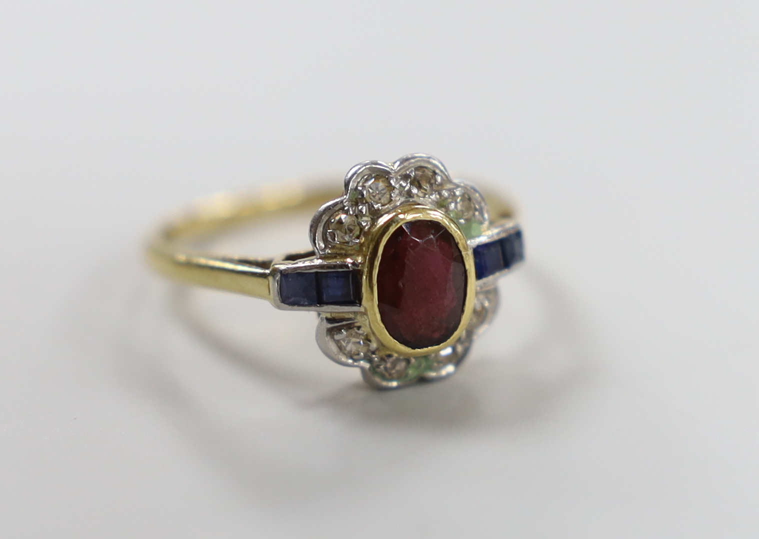 A 1920's/1930's yellow metal, ruby, sapphire and diamond set oval cluster ring, size O, gross weight