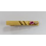 A modern 18k, ruby and diamond set three stone tie clip, 47mm, gross weight 7.7 grams.